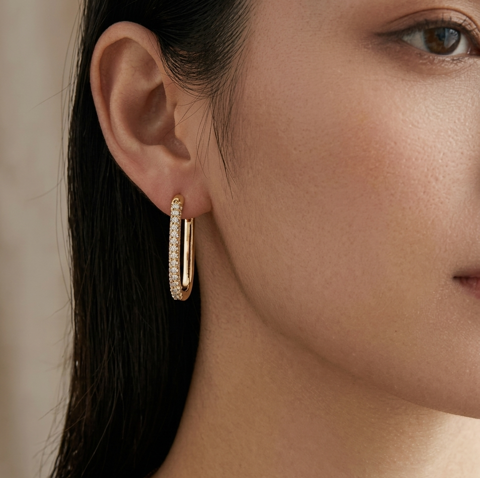 Gold iced out oval loop hoop earring worn on person's ear