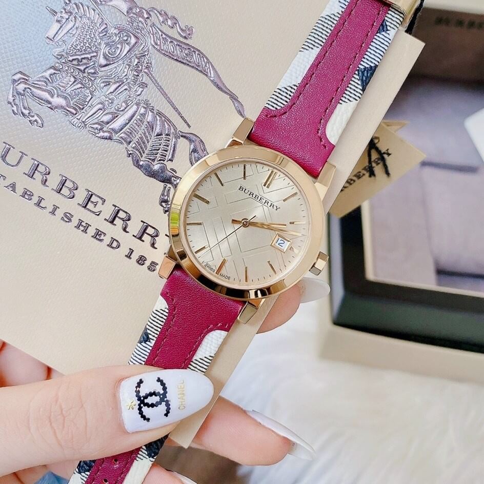 Burberry The City watch on wrist with gold-tone case and pink striped leather strap