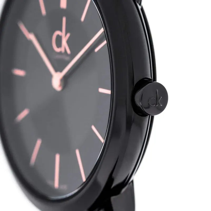 Close-up detail of Calvin Klein watch dial with rose gold hour markers and hands on black background