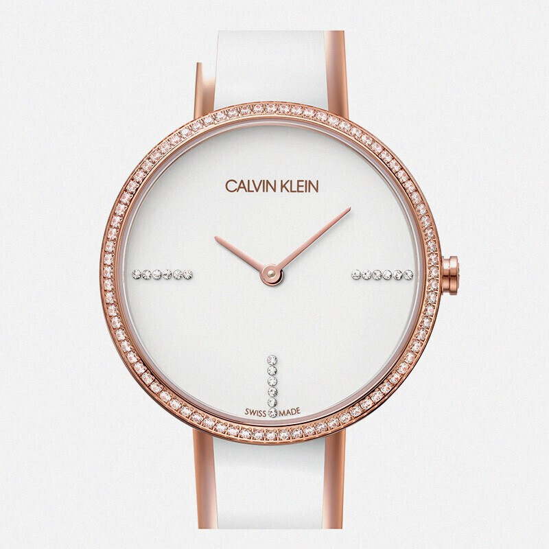 Close-up of white dial face showing Calvin Klein branding, crystal markers, and rose gold hands