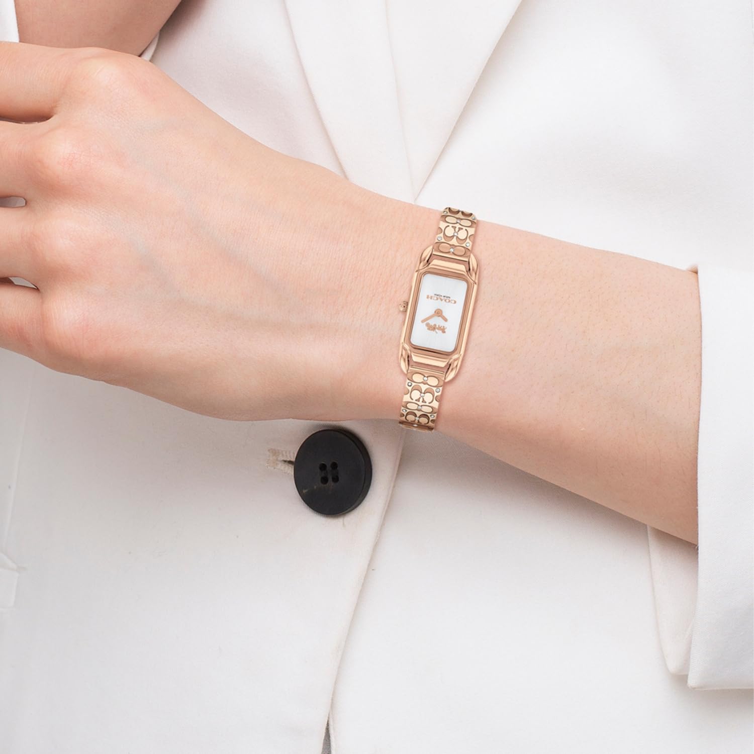Coach Cadie rose gold rectangular watch worn on wrist over white sleeve