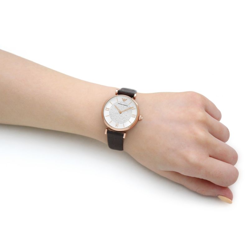 Women's rose gold watch with white crystal pave dial and brown leather strap worn on wrist