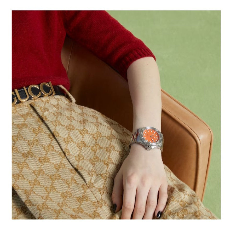 GUCCI Dive watch with orange dial worn on wrist, styled with red sweater and beige bag