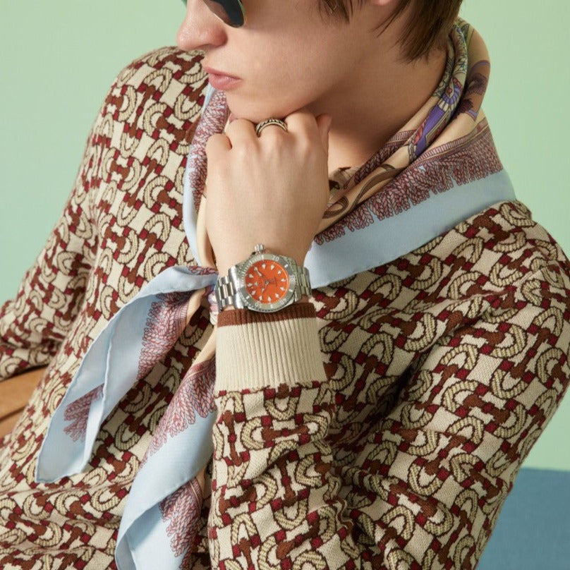 GUCCI Dive watch with orange dial worn on wrist against patterned fabric background