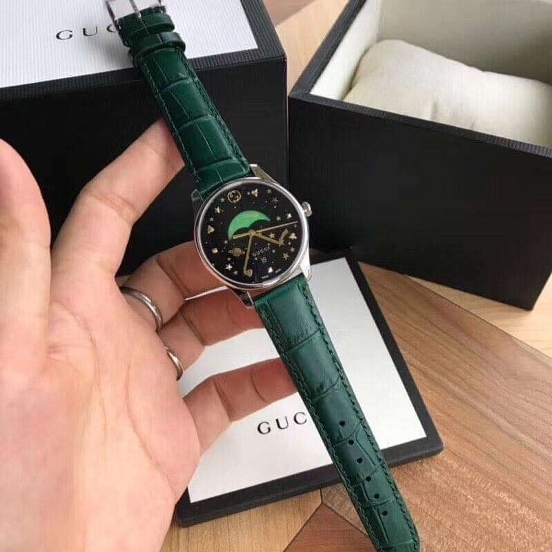 Gucci G-Timeless watch on wrist showing black dial with gold markers and green crocodile leather strap