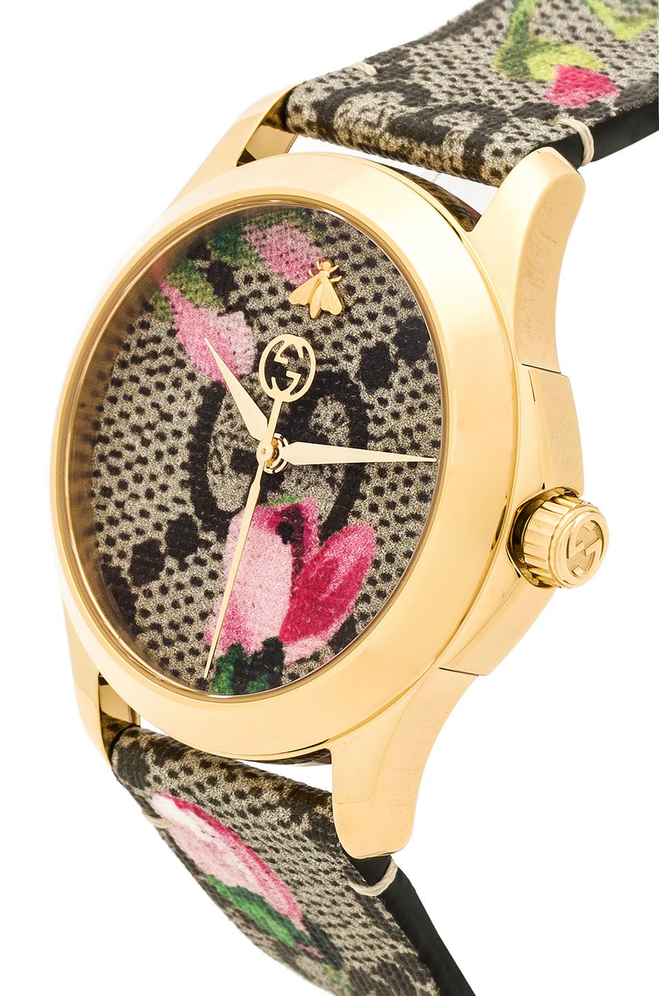 Gucci G-Timeless watch side angle showing gold case, pink bloom print, and canvas strap