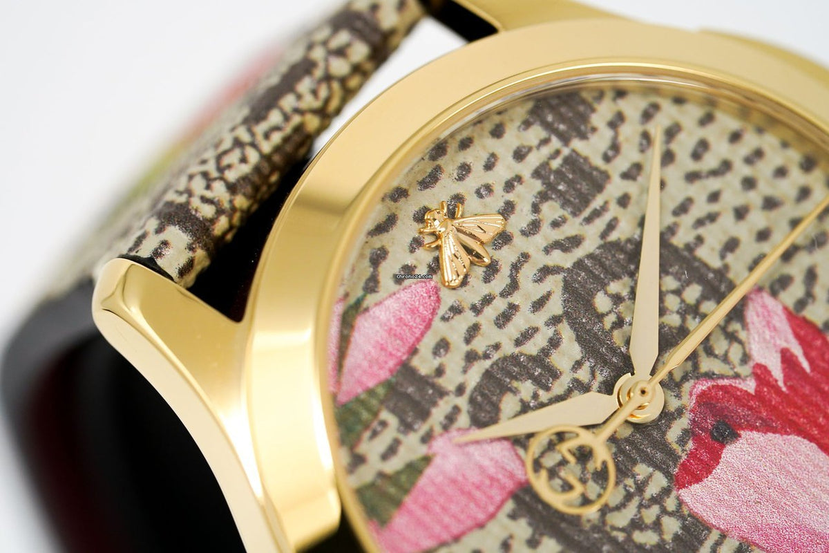 Close-up detail of pink and green floral print dial with gold hands and Gucci logo
