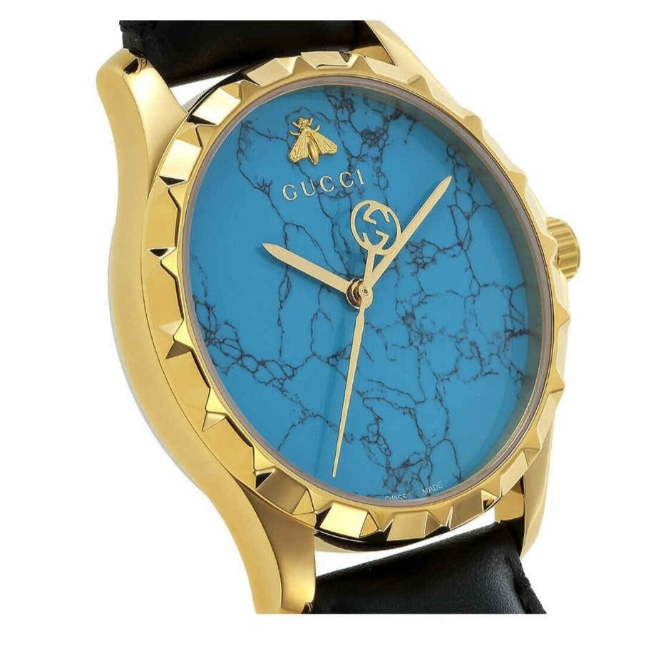 Gucci G-Timeless watch side profile displaying gold case, black leather strap, and dial detail