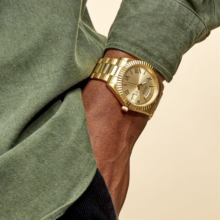 Guess Connoisseur gold tone watch worn on wrist with green sleeve