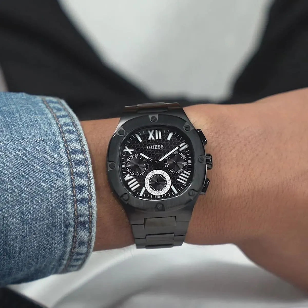 GUESS GW0572G3 black multi-function watch worn on wrist with blue denim cuff