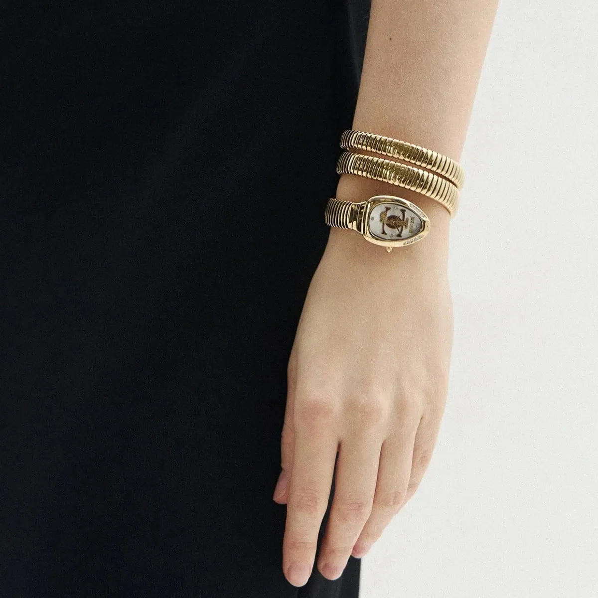 Gold watch with triple-wrap snake band worn on wrist against black clothing