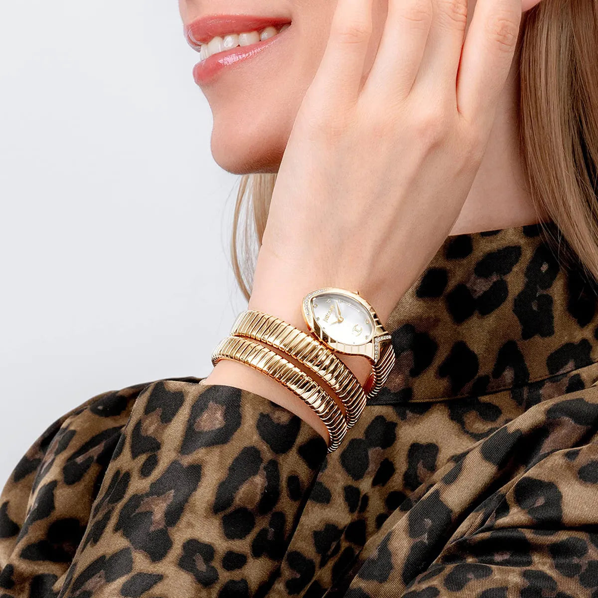 Just Cavalli snake watch worn on wrist with gold bracelet and oval white dial