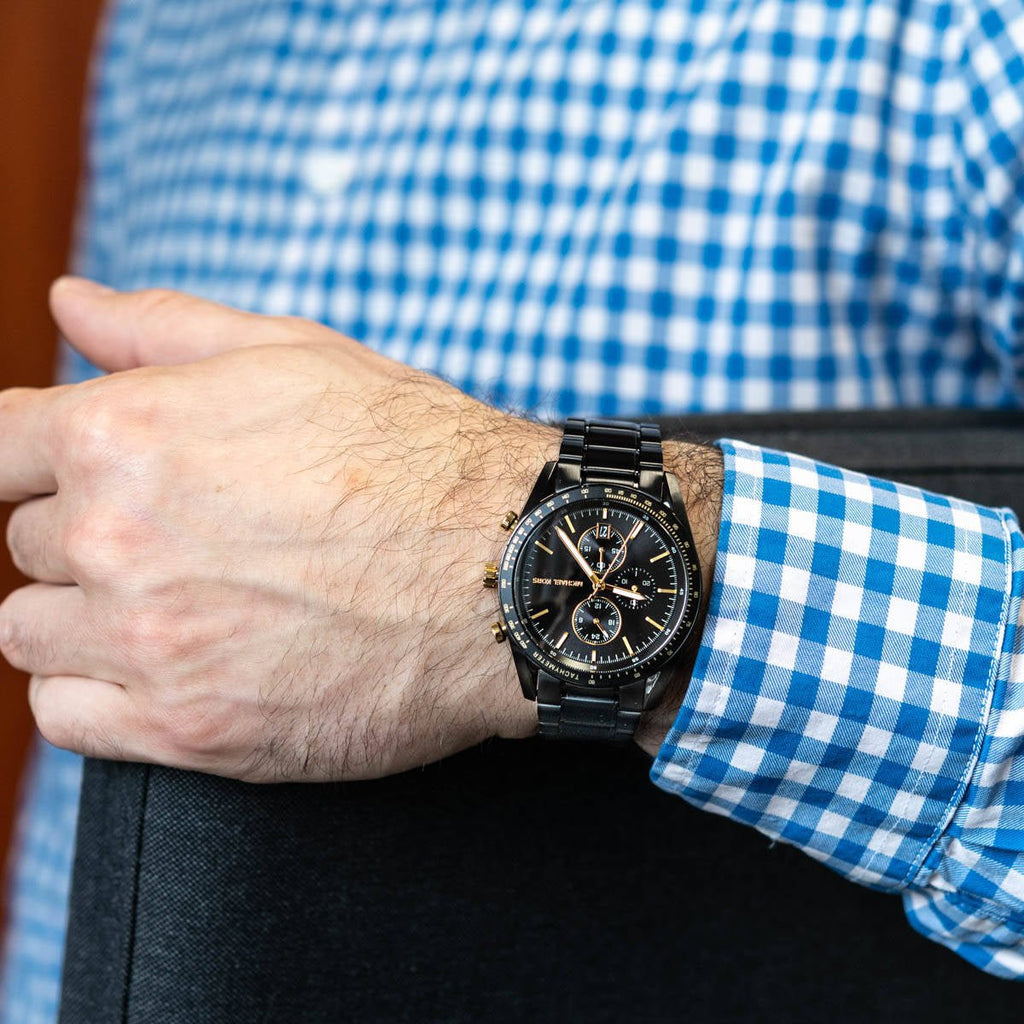 Michael Kors Accelerator MK9113 black chronograph watch worn on wrist with blue shirt
