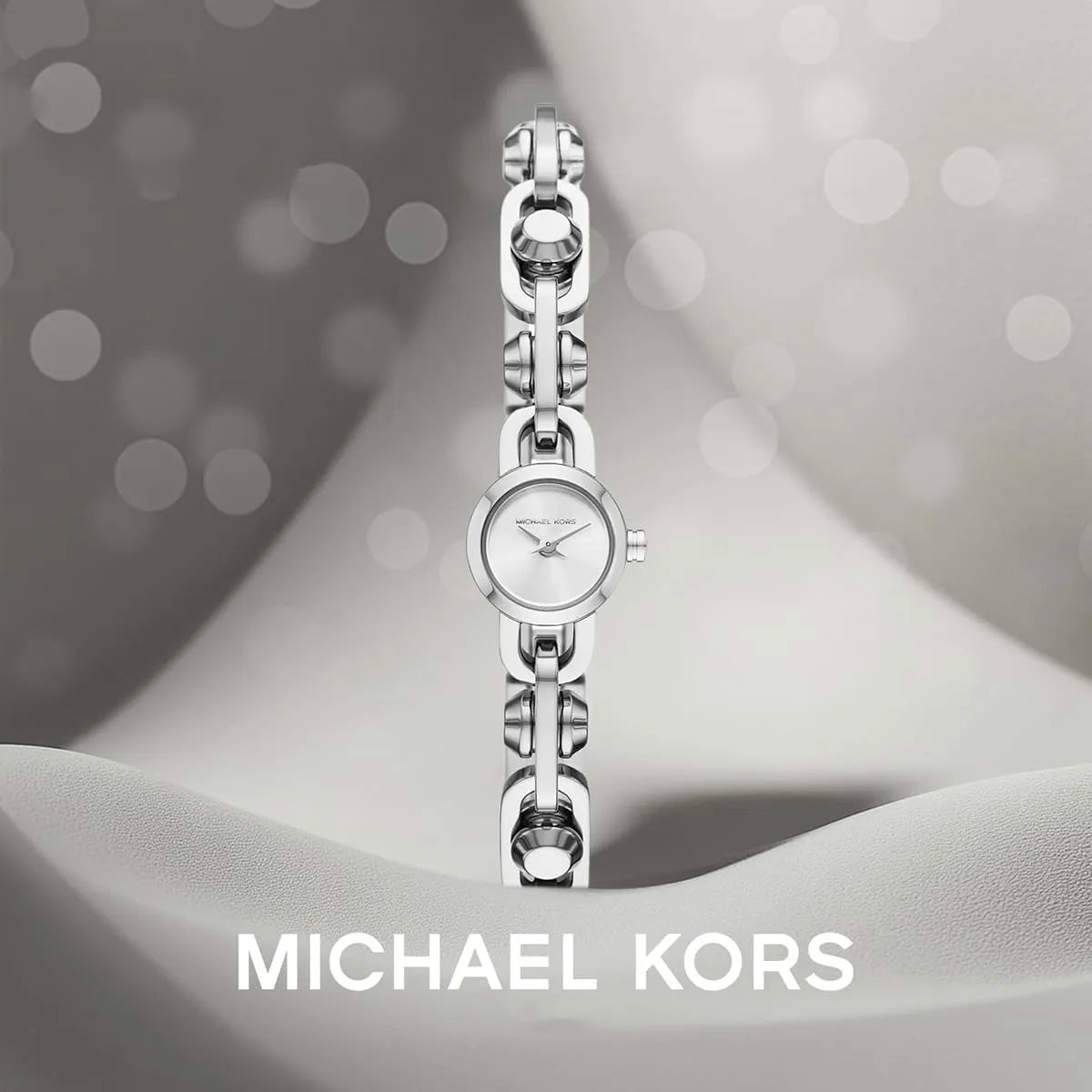 Michael Kors Mini Astor Link silver-tone bracelet watch on wrist with branded background