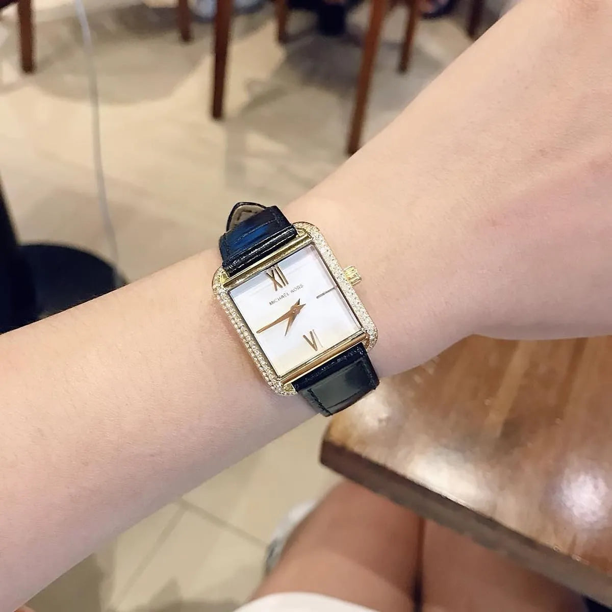Wrist view of Michael Kors Lake MK2762 women's watch with white dial and black leather strap