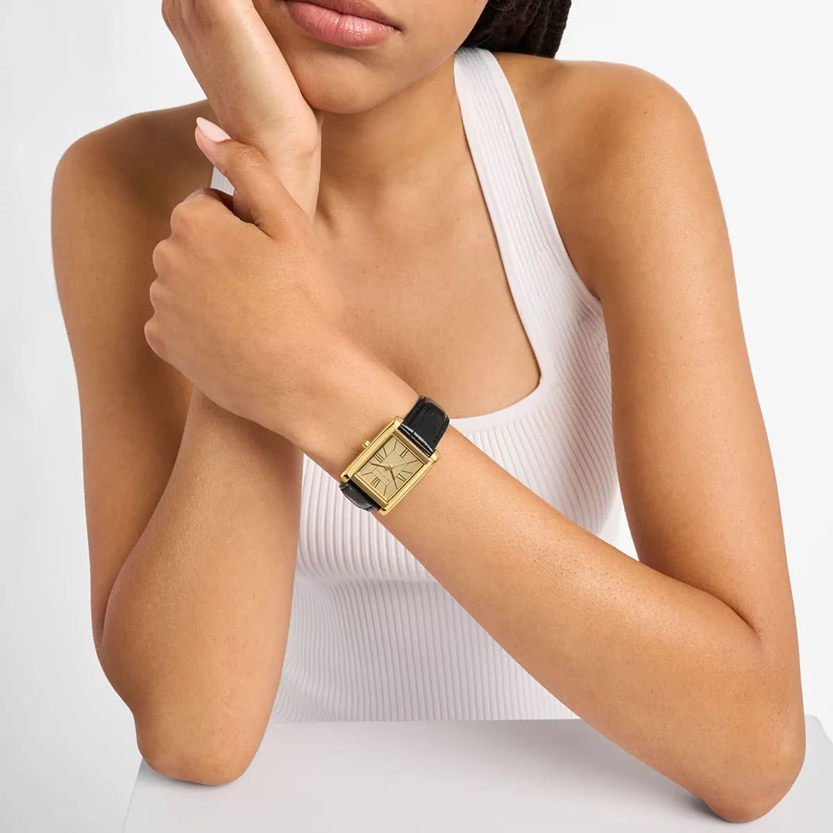 Essex watch worn on woman's wrist with gold rectangular case and black leather strap