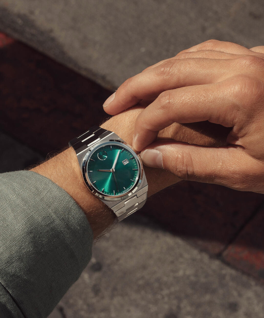 Movado BOLD Quest stainless steel men's watch on wrist displaying teal green dial