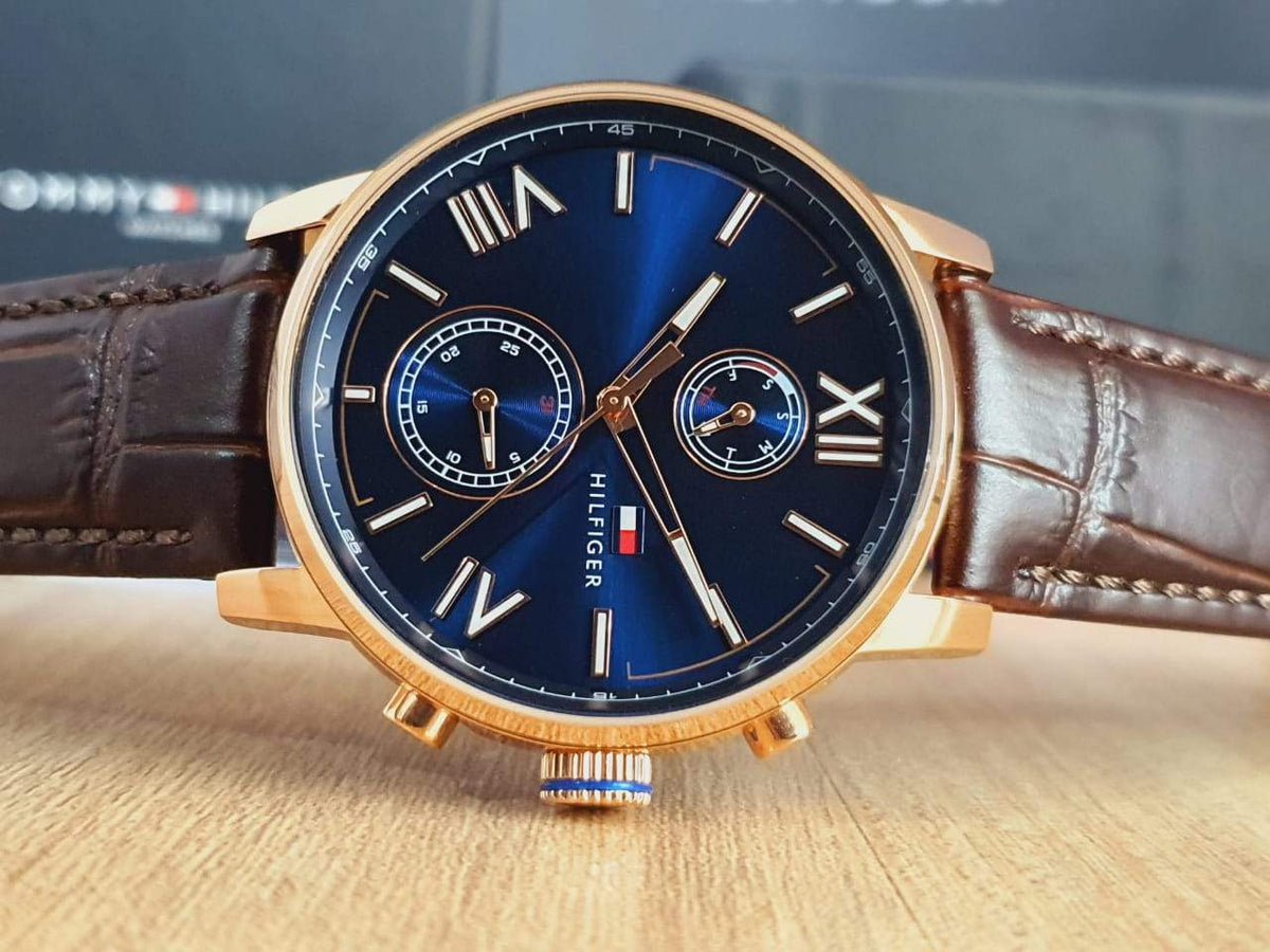 Angled side view of Tommy Hilfiger watch on brown leather strap showing blue dial and rose-gold case