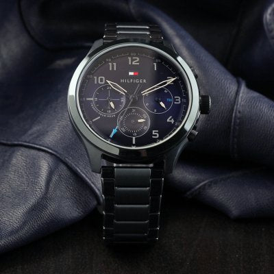 Tommy Hilfiger blue chronograph men's watch worn on wrist with dark metal bracelet