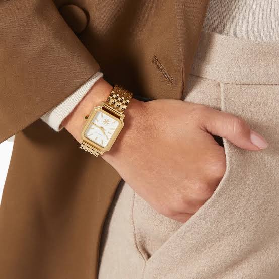 Tory Burch Robinson gold stainless steel watch worn on wrist with neutral layered clothing