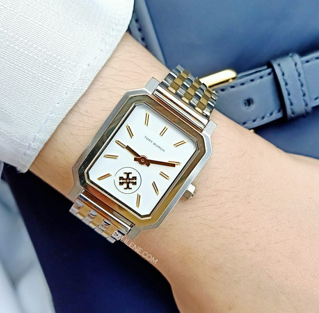 Tory Burch Robinson two-tone gold watch worn on wrist with white cuff and navy leather strap