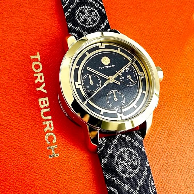 Tory Burch chronograph watch on wrist displaying navy fabric strap and gold-tone case against orange background