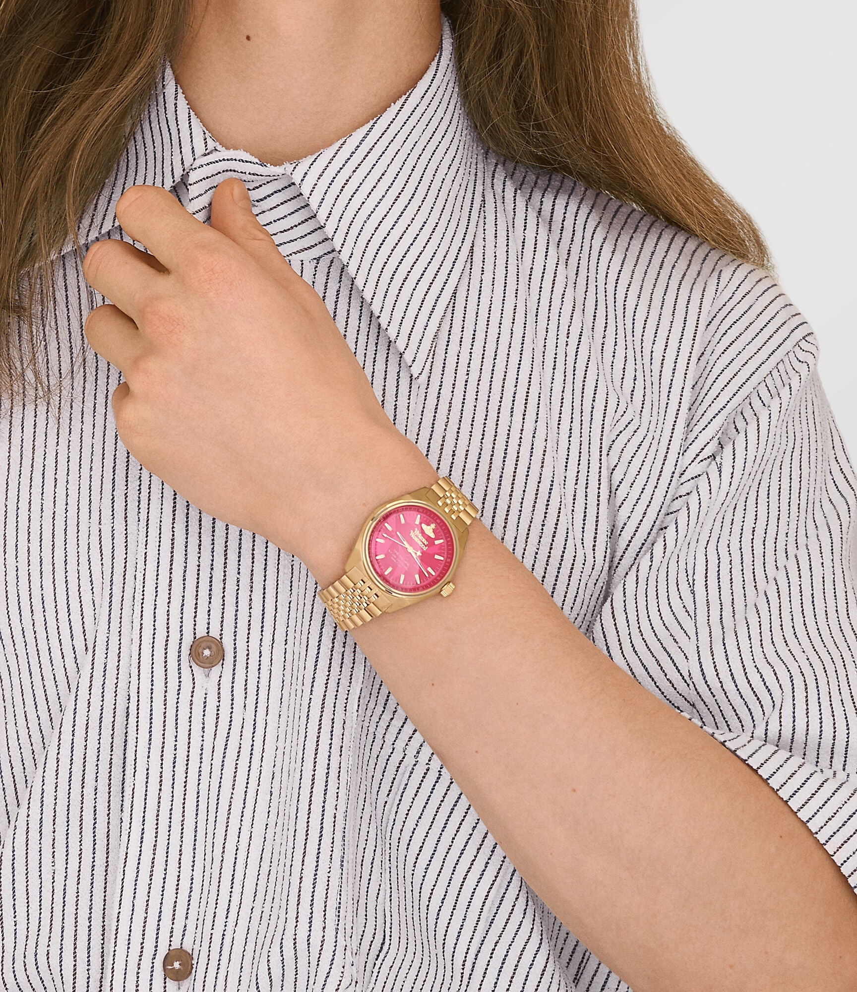 Close-up of Vivienne Westwood Lady Sydenham gold watch with hot pink dial on wrist