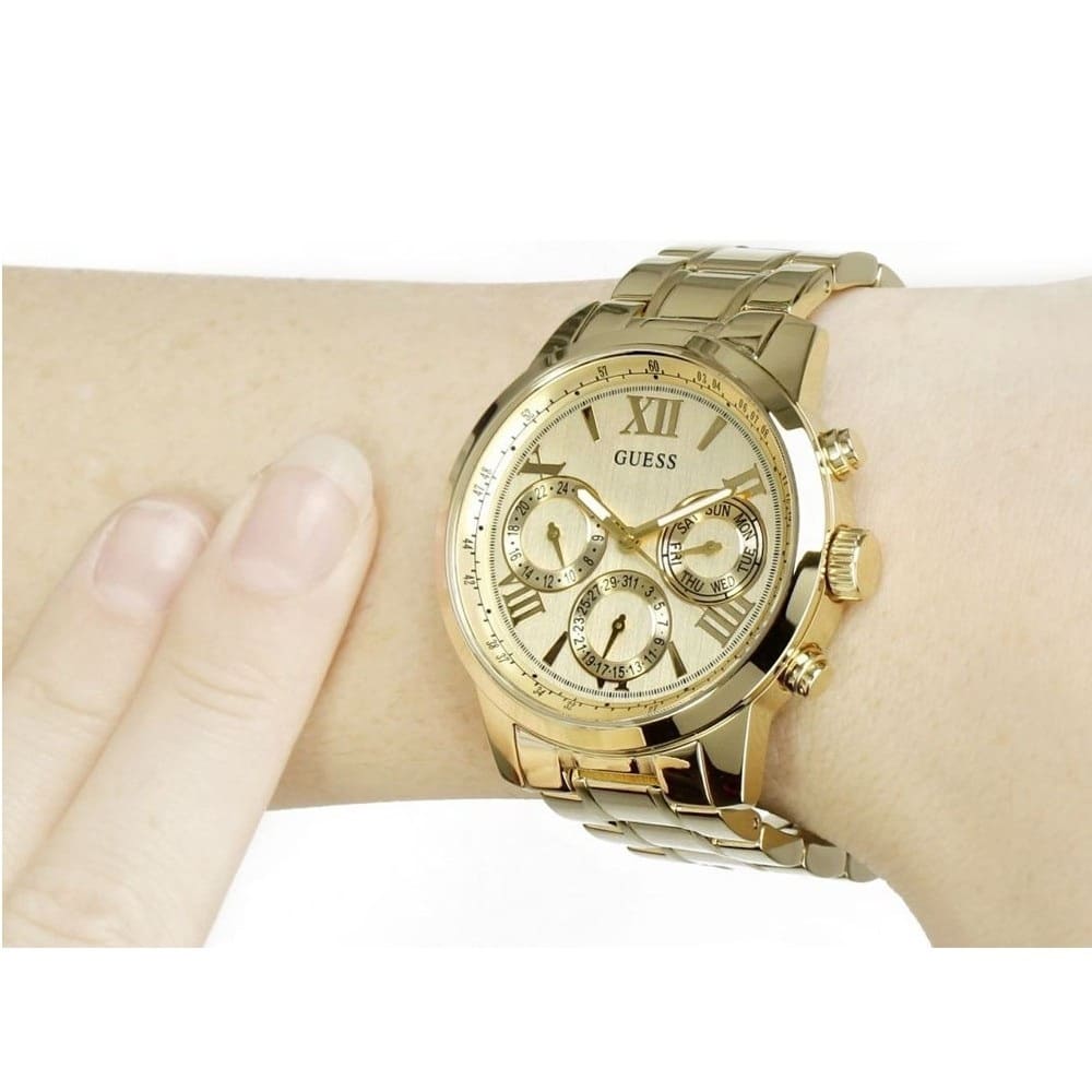 Guess Sunrise gold tone multifunction watch worn on wrist with gold link bracelet